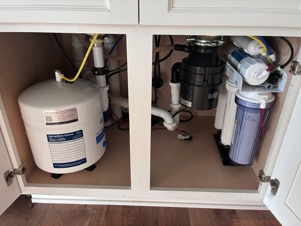 Completed reverse osmosis install with storage tank and filter bank inside a white kitchen cabinet